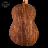 The back of an acoustic guitar made of rich, dark brown wood with prominent grain patterns, shown against a solid black background with a Tone Shop watermark in the top left corner.