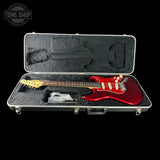 Red electric guitar in a black case with 'Tone Shop' logo.