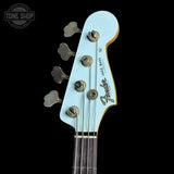 Close-up of a Fender Jazz Bass headstock in a light mint green finish with gold hardware, set against a solid black background. A Tone Shop watermark is visible in the top left corner.