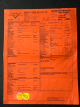 An orange Pineridge 'Shop Floor Traveler' instrument transfer form with printed text fields, barcodes, and a yellow circular sticker, photographed flat against a dark background.