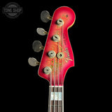 Close-up of a vintage Fender Jazz Bass headstock in a faded red finish with gold and green decorative graphics, four metal tuning pegs, and the Fender logo on a black background.