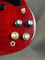 Close-up of a red electric guitar with control knobs on a gray background