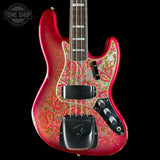A Fender Jazz Bass with a vibrant red body and a detailed paisley pickguard featuring pink, green, and gold swirls. The guitar is shown against a solid black background with a Tone Shop logo in the top-left corner.