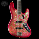 A Fender Jazz bass guitar with a pink and red body, covered in a green paisley pattern. The neck is dark wood with silver block inlays, and the headstock is cropped out against a solid black background.