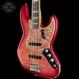 A Fender Jazz bass guitar with a vibrant red body featuring a detailed paisley pattern in pink, green, and gold. The neck is dark wood, and the headstock is partially visible at the top edge.