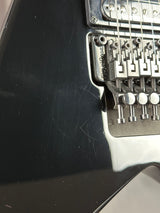 Close-up of a guitar's bridge and tuning pegs on a black guitar body.