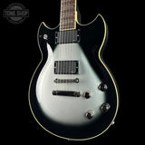 Electric guitar with a silver and black finish on a black background, featuring the Tone Shop logo.