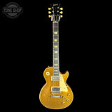 A Gibson Les Paul Custom electric guitar in a distressed gold finish, shown against a solid black background. The headstock features the Gibson logo, and the neck has gold inlays.