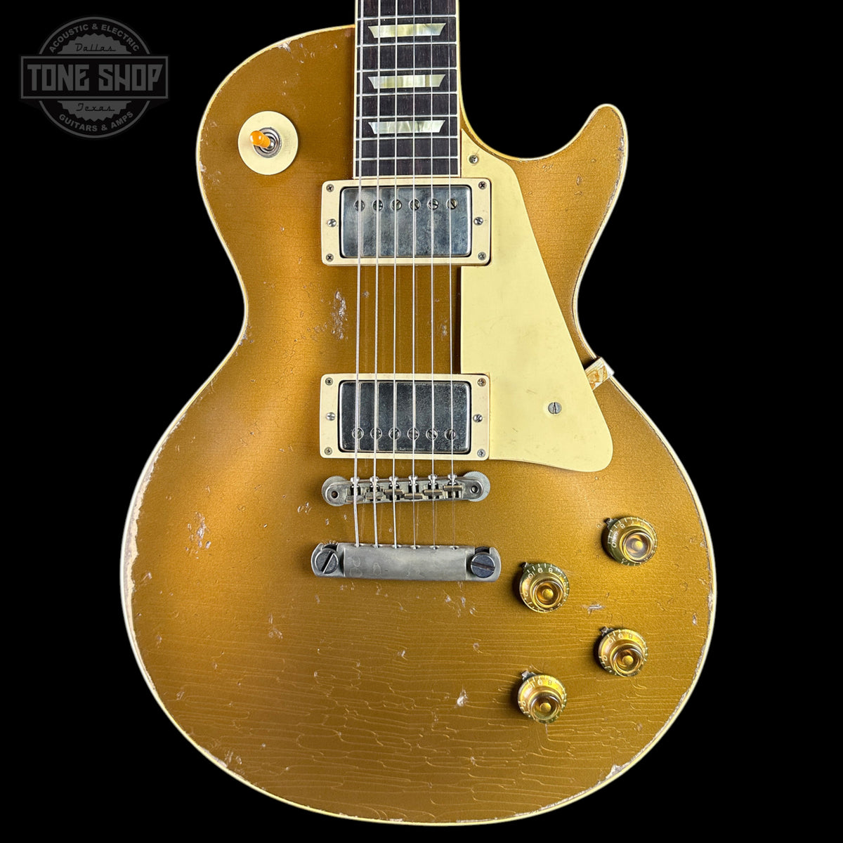 A classic electric guitar with a distressed gold finish, featuring a cream pickguard, dual humbucker pickups, and gold-toned control knobs, shown against a solid black background.