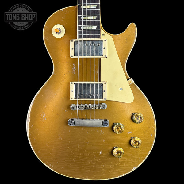 A classic electric guitar with a distressed gold finish, featuring a cream pickguard, dual humbucker pickups, and gold-toned control knobs, shown against a solid black background.