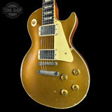 A classic electric guitar with a distressed gold finish, featuring a cream pickguard, dual humbucker pickups, and gold-toned control knobs, shown against a solid black background.
