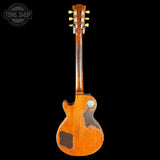 A vintage electric guitar shown from the back, featuring a heavily worn orange-brown finish with significant dark scuffs and scratches, set against a solid black background.