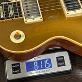 Close-up of a gold-finish electric guitar body resting on a digital scale showing 8.15 lbs, with the guitar pickups and part of the neck visible.