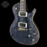 A close-up studio shot of an electric guitar body and neck against a black background. The guitar has a dark blue-gray flamed maple top with a subtle wood grain, gold hardware, and white control plates.