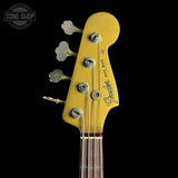 Close-up of a Fender Jazz Bass headstock in metallic gold, featuring four silver tuning pegs with flower-shaped tops, a dark wood fretboard, and the Fender logo on a solid black background.