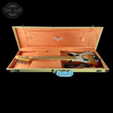 A sunburst Fender Stratocaster electric guitar resting inside an open cream-colored hard case with a peach-pink lined interior. The Fender logo is visible on the inside lid, and a blue cloth is placed below the handle.