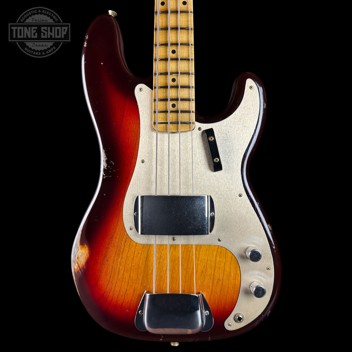 A classic Fender Strat-style electric bass guitar with a sunburst finish, featuring a natural maple neck, white pickguard, and black hardware, shown against a solid black background with a Tone Shop watermark in the top left corner.