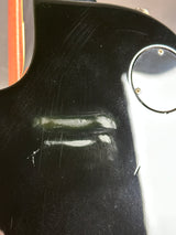 Close-up of a black guitar with visible scratches and a reflection.