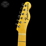 Close-up of a Fender Telecaster electric guitar headstock in a natural maple finish, showing six tuning pegs and the Fender Telecaster logo, set against a solid black background.