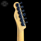 Close-up of the headstock of an electric guitar with a natural maple wood finish and dark blue tuning pegs, shown against a solid black background with a Tone Shop watermark in the top left corner.