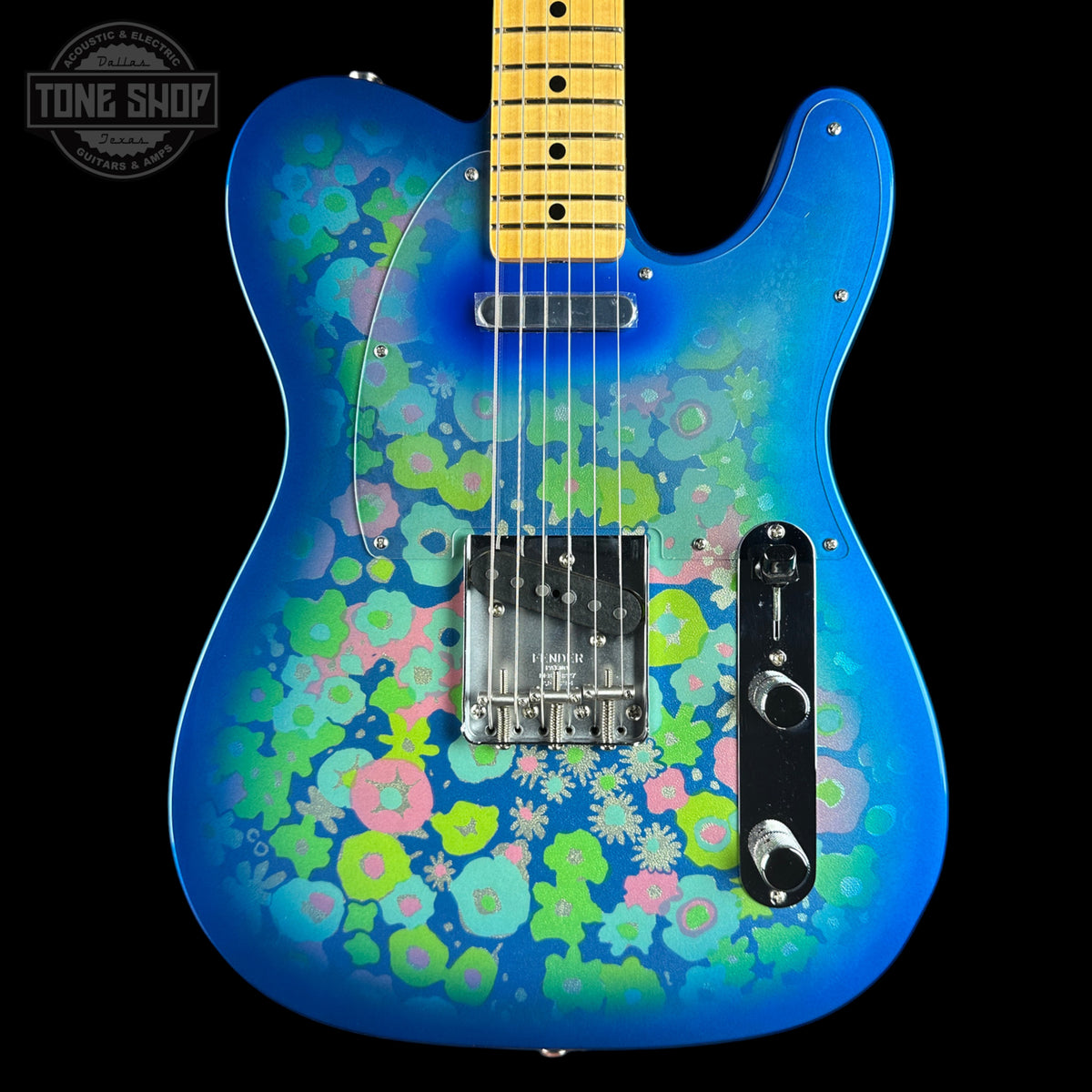 A blue electric guitar with a vibrant pink, green, and blue floral pattern on the body, shown against a solid black background. The neck is a natural maple wood color with black frets.