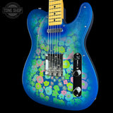 A blue electric guitar with a vibrant psychedelic floral pattern in pink, green, and blue, featuring a yellow maple neck and chrome hardware, shown against a black background with a Tone Shop logo in the top left corner.