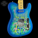 A blue electric guitar with a vibrant floral pattern in pink, green, and yellow on the body, featuring a natural maple neck and chrome hardware, shown against a black background with a Tone Shop watermark.