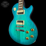 Turquoise electric guitar with gold hardware on a black background, featuring 'Tone Shop' logo.