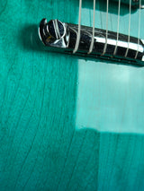 Close-up of a guitar's fretboard and tuning pegs on a teal background