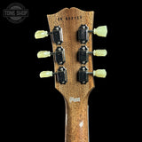 Close-up of the headstock of an electric guitar against a black background, showing six black tuners with pale yellow-green pegs, a brown wood grain finish, and 'Tone Shop' branding on the back.