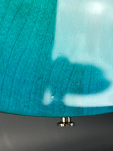 Close-up of a turquoise ceramic plate with a metallic handle on a gray background