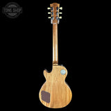 A classic electric guitar shown from the back, featuring a natural wood body with a visible grain, a dark brown pickguard, and a round chrome badge on the upper back. The headstock is turned upside down against a solid black background, with a 'TONE SHOP' watermark in the top-left corner.