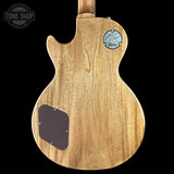 The back of a Gibson Les Paul Custom electric guitar, showcasing a natural wood grain finish and a blue Gibson logo patch on a black background.
