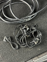 A bundle of black audio or video cables with various connectors, including banana plugs and adapter plugs, coiled on a dark textured surface.
