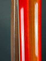 Close-up of a glossy wooden guitar body showing a vibrant red-orange finish with visible wood grain and a dark background.