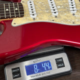 Red electric guitar on a digital scale displaying weight