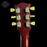 Close-up of the headstock of a vintage electric guitar, showing a glossy dark red wood finish, six cream-colored tuning pegs, and gold-toned tuning machines against a solid black background.