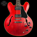 A red electric guitar with a black pickguard, dual humbucker pickups, and chrome hardware, shown against a black background with a Tone Shop watermark in the top left corner.