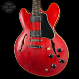 A red electric guitar with a black pickguard and black controls, photographed against a black background. A Tone Shop watermark is visible in the top-left corner.