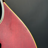 Close-up detail of a red acoustic guitar body showing the edge of the soundhole and a small scratch on the finish, set against a dark gray background.
