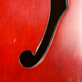Close-up of a red wooden f-hole, likely on a violin or cello, showing the glossy red wood grain and black edge trim.
