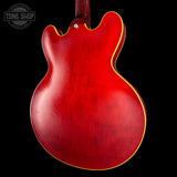 Close-up of the back of a red electric guitar body with a yellow binding edge, shown against a black background. A Tone Shop watermark is visible in the upper left corner.