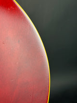 Close-up of a red guitar body edge with a thin yellow binding line against a dark gray background.