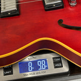Close-up of a red electric guitar body resting on a digital scale displaying 8.98 oz, with the scale showing part of its silver body and buttons.