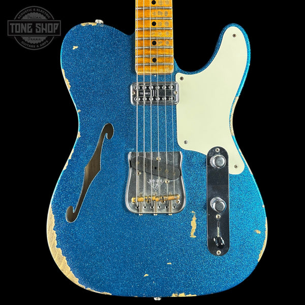 Blue electric guitar with a worn finish on a black background, featuring the Tone Shop logo.