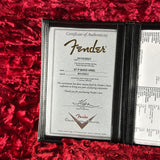 A Fender bass headstock authenticity certificate displayed inside an open black folder on a textured red velvet background. The certificate is dated 01/12/2023 for a 57 P Bass Hrel, and the right page shows additional certification details.