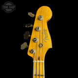 Close-up of a Fender bass guitar headstock in a natural wood finish with gold-toned tuning pegs and strings, shown against a solid black background. A 'TONE SHOP' watermark is visible in the top-left corner.