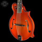 A close-up studio shot of a mandolin against a solid black background, featuring a vibrant orange glitter finish with black pickguard and trim. A Tone Shop watermark is visible in the top left corner.