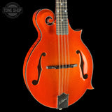 A close-up studio shot of a mandolin against a solid black background. The mandolin has a vibrant orange glitter finish on its body, with a dark fretboard, black truss rod cover, and a Tune Shop logo watermark in the upper left corner.