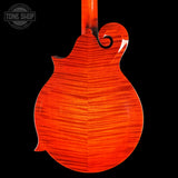 Close-up of the back of a mandolin with a glossy orange-red flamed maple wood finish, shown against a solid black background. A Tone Shop watermark is visible in the top-left corner.